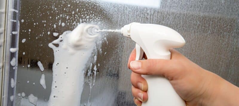 closeup of a spray bottle spraying cleaning solution on a mirror to clean it