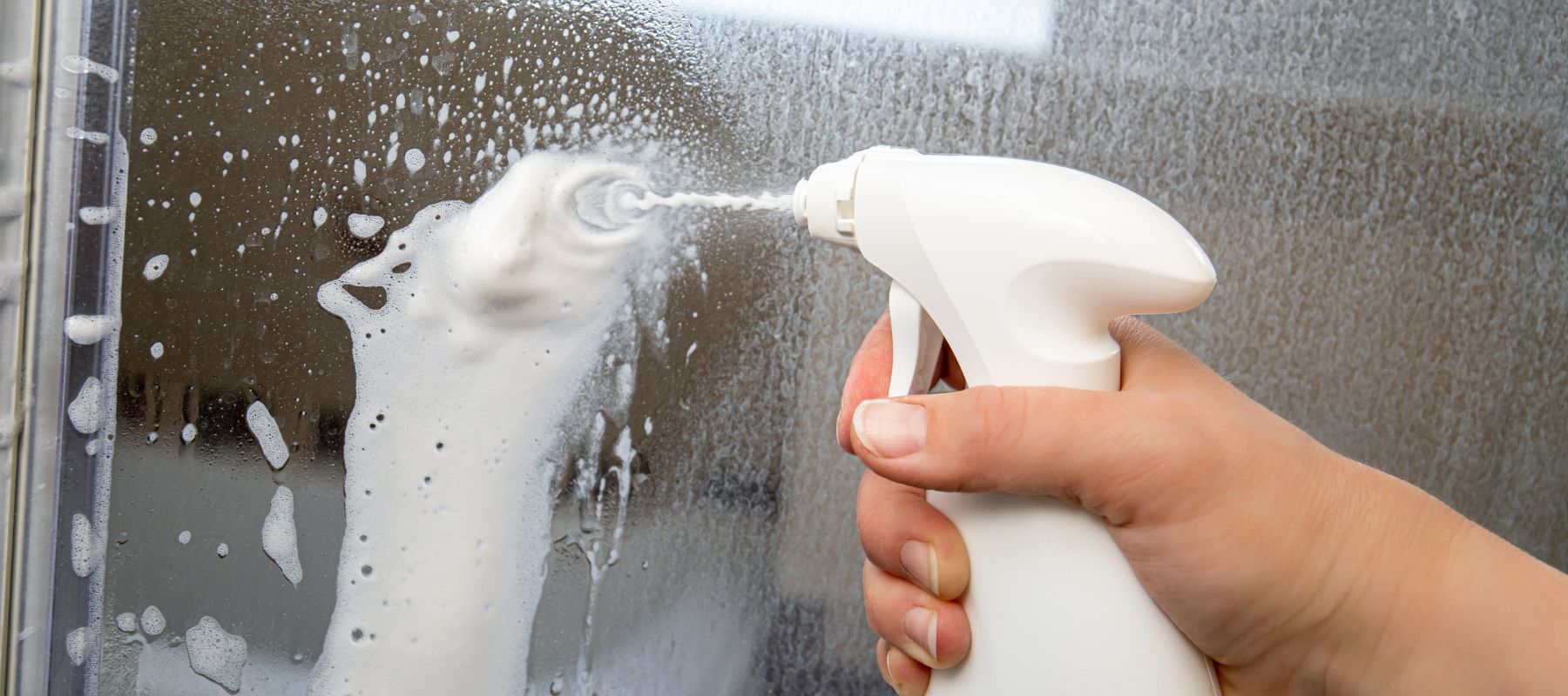 closeup of a spray bottle spraying cleaning solution on a mirror to clean it