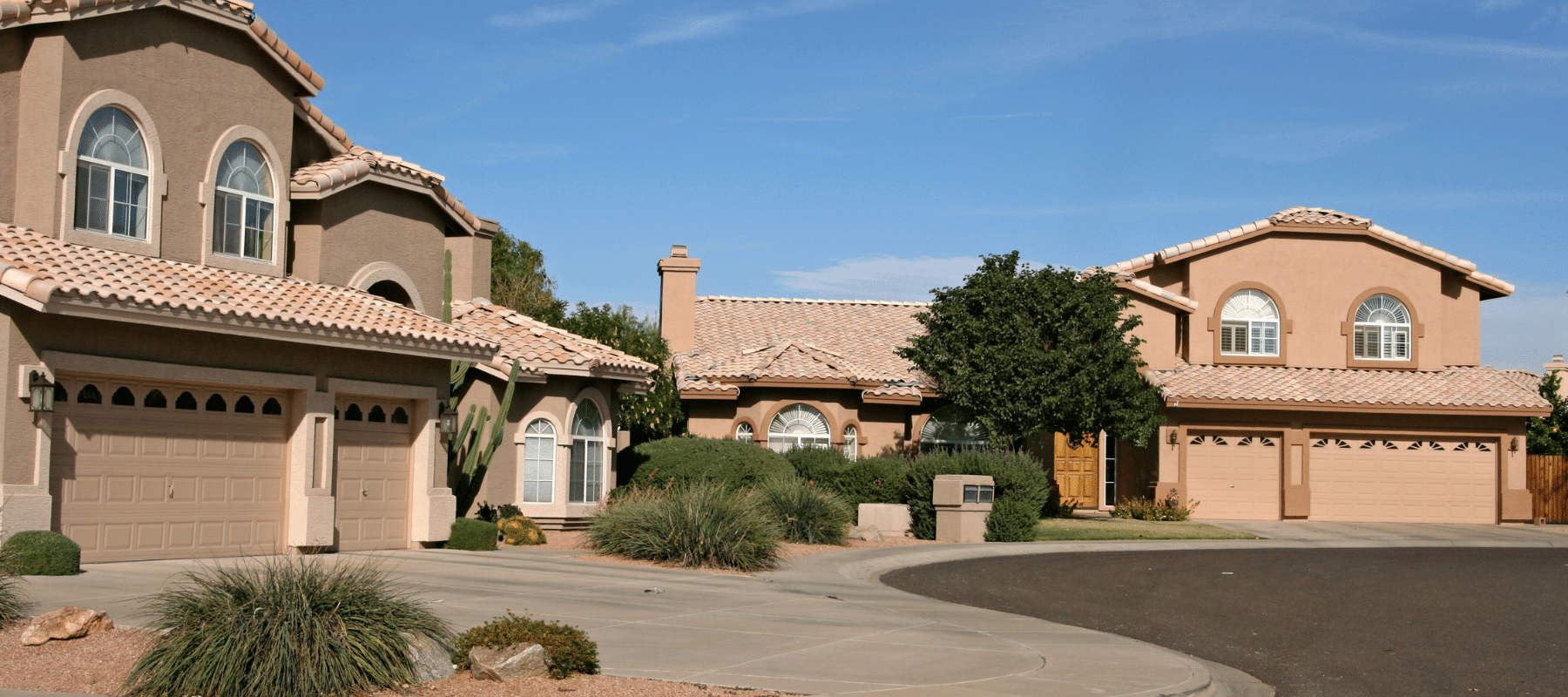 A view of a suburban cul-de-sac featuring stucco houses with clay-tiled roofs and desert landscaping
