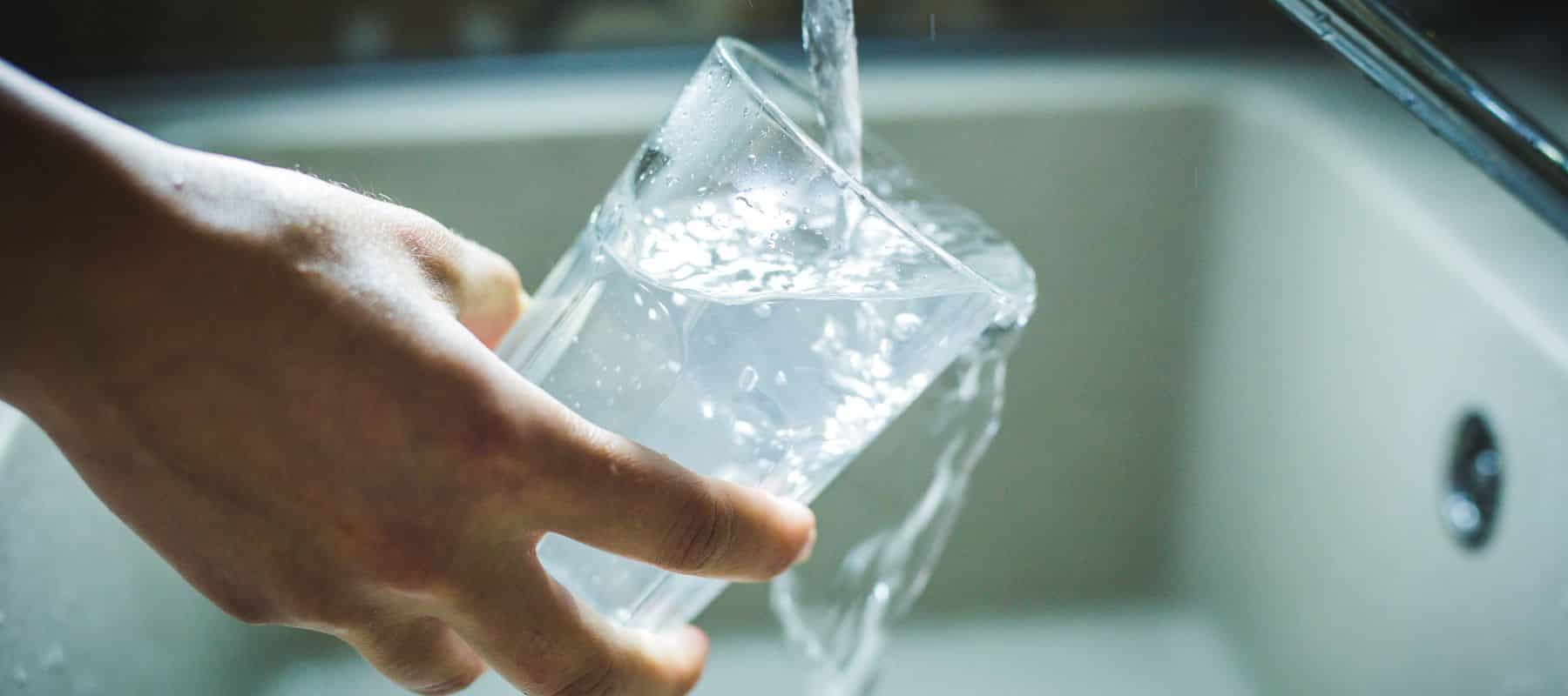 A person's hand holds a glass being filled with clear water from a faucet over a sink
