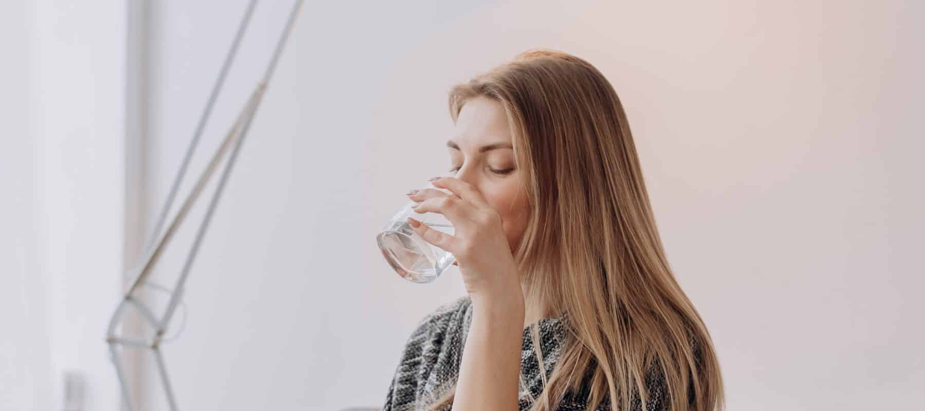 closeup of a woman drinking water from a glass cup in the comfort of her living room