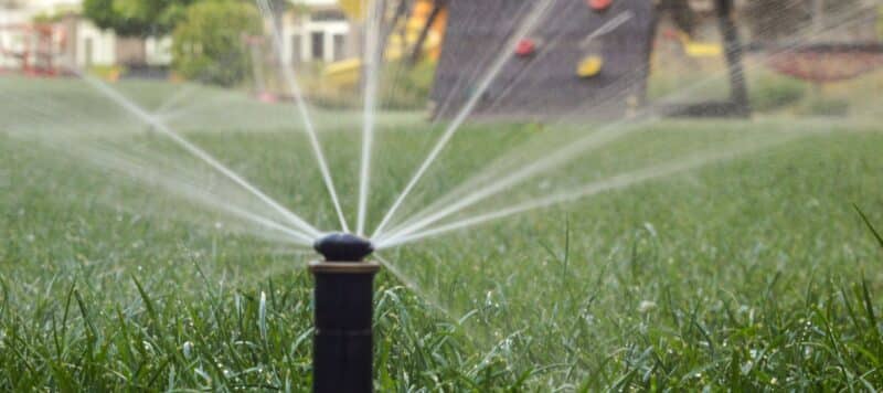 Close-up of a lawn sprinkler spraying water across green grass
