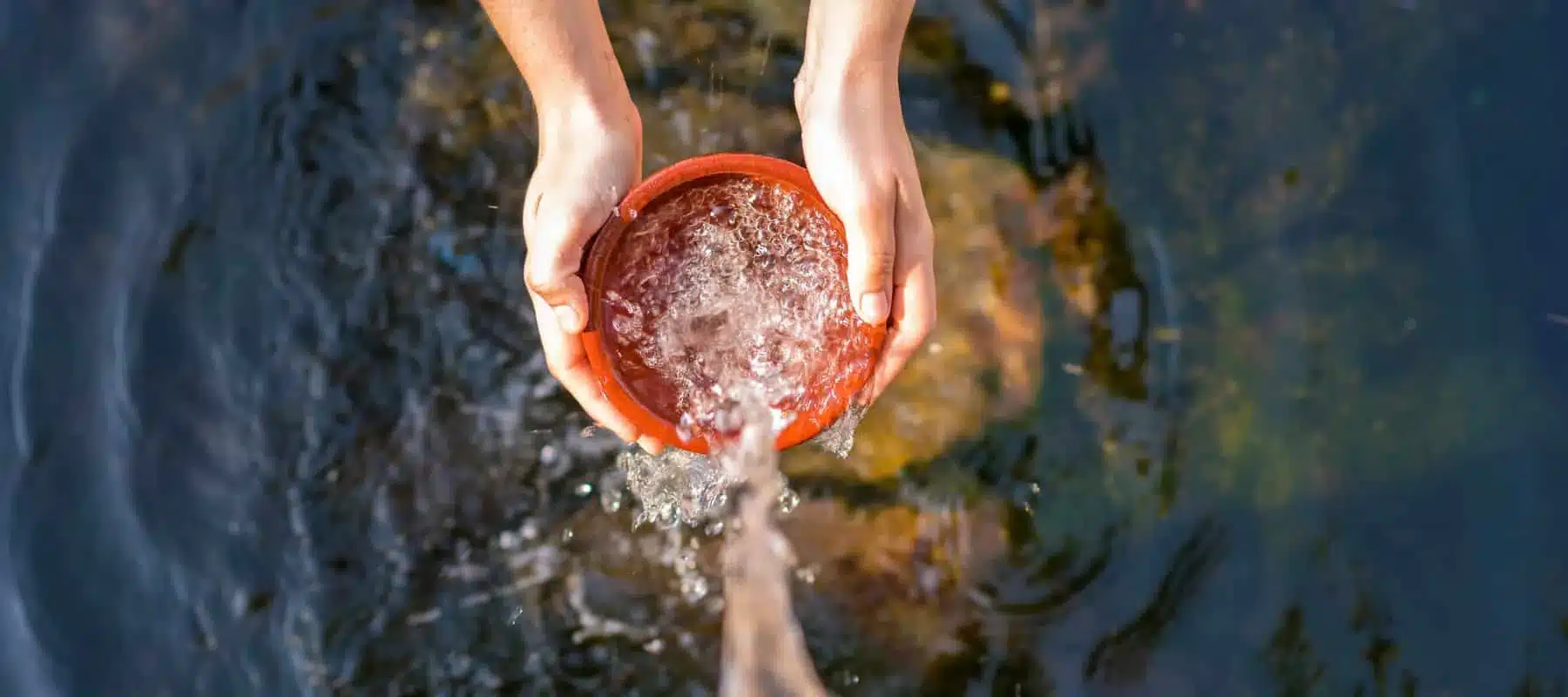 top view of hands holding a red bowl with water falling from the sky into the bowl
